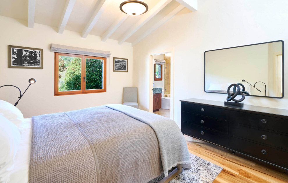 A plush bed faces a black dresser with a mirror on top